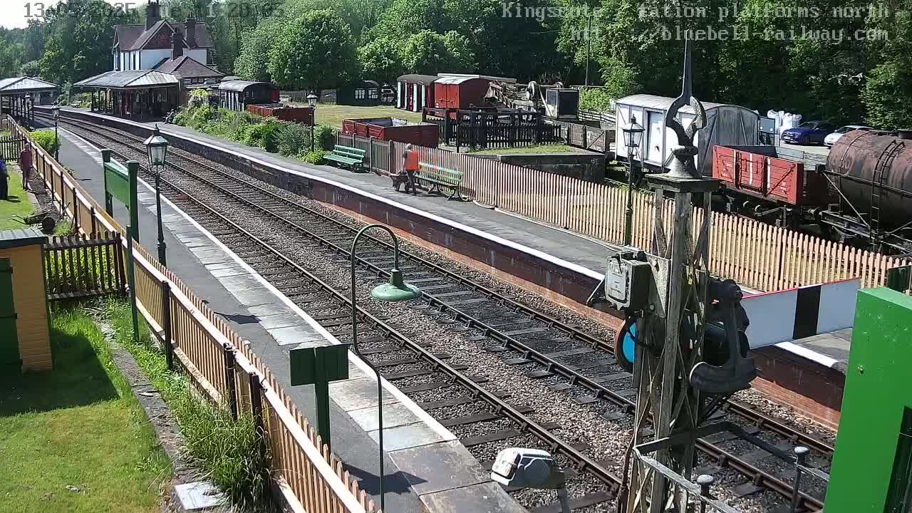 A sunny day at a train station with multiple train cars and a platform alongside several train tracks.