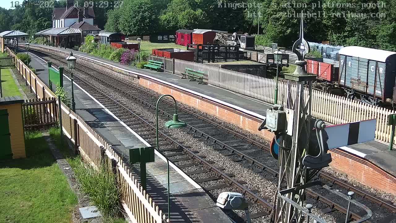 A sunny day at a railway station with train tracks, platforms, and several freight cars visible.