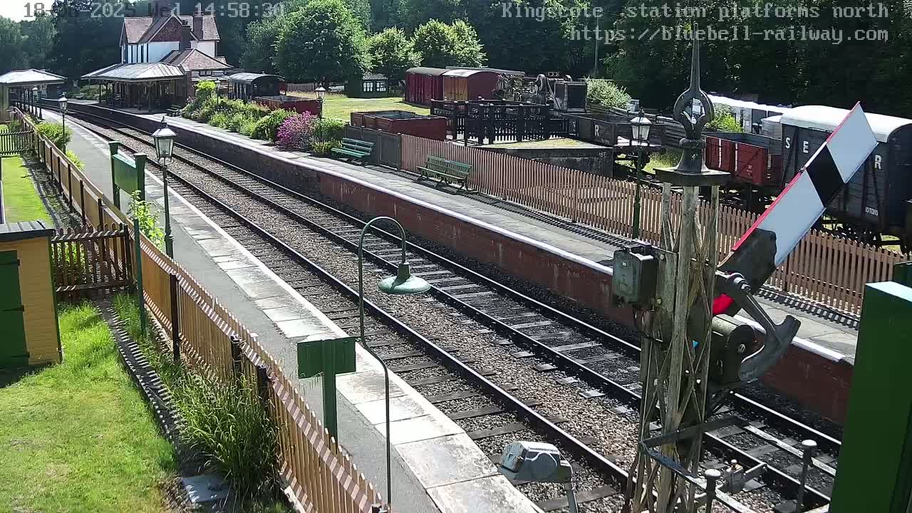 A sunny view of a train station platform with several railway cars and a signal lever visible.