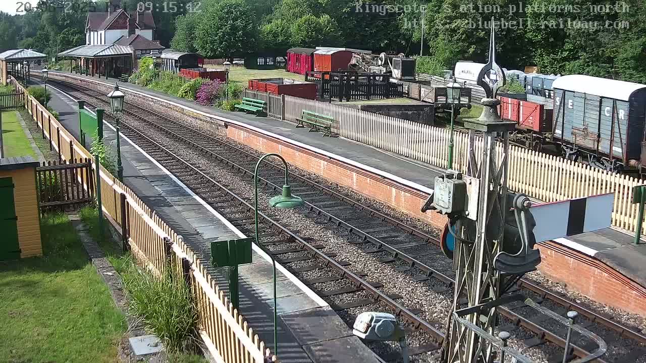 A sunny day at a train station with multiple railway tracks, several railway cars, and a station building.