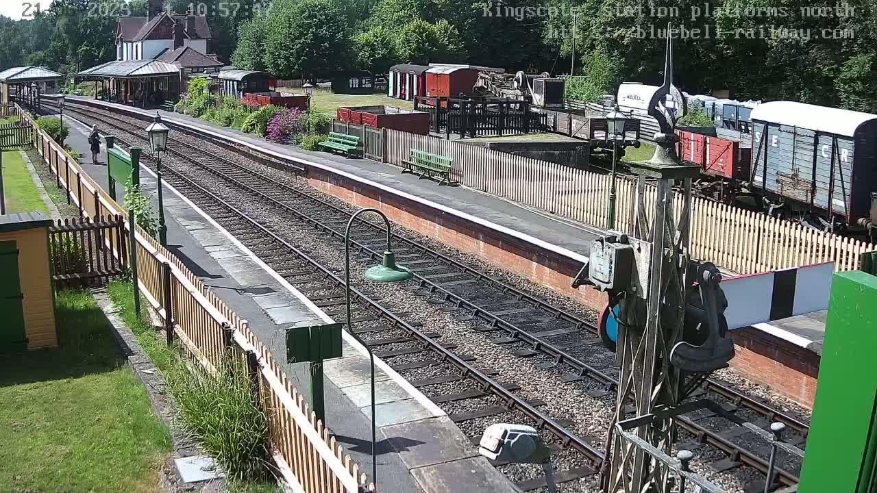 A sunny day at a train station with multiple train cars visible on the tracks and a person walking on the platform.