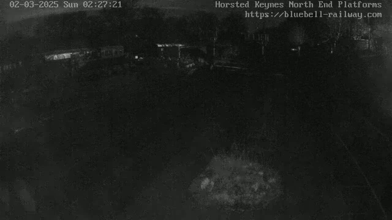A low-light nighttime image shows a dark, mostly empty area with some indistinct structures in the background.