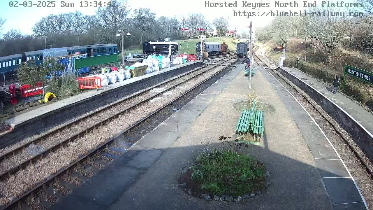 A sunny day at a train station with several railway cars, some construction materials, and a few people.