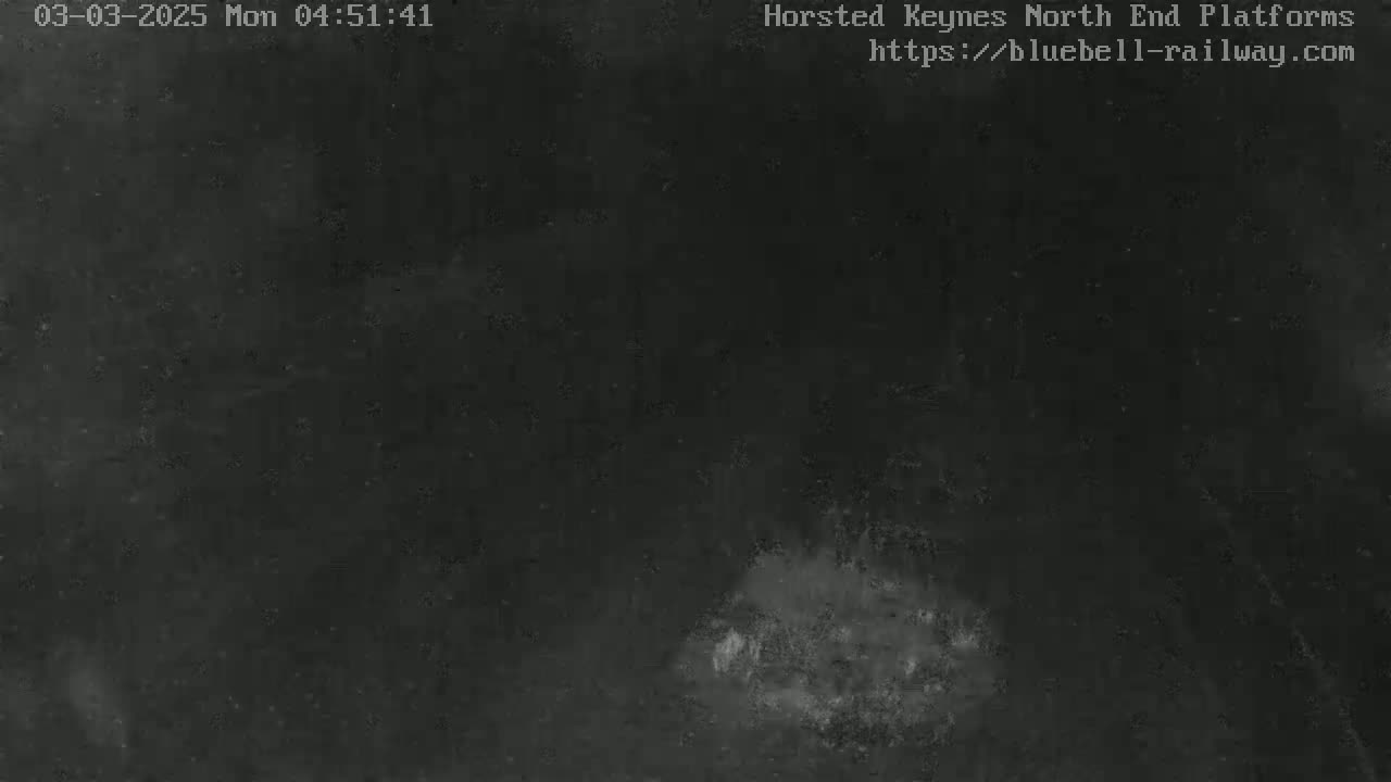 A dark, low-light nighttime image shows a mostly black scene with a small, lighter gray area in the bottom center.