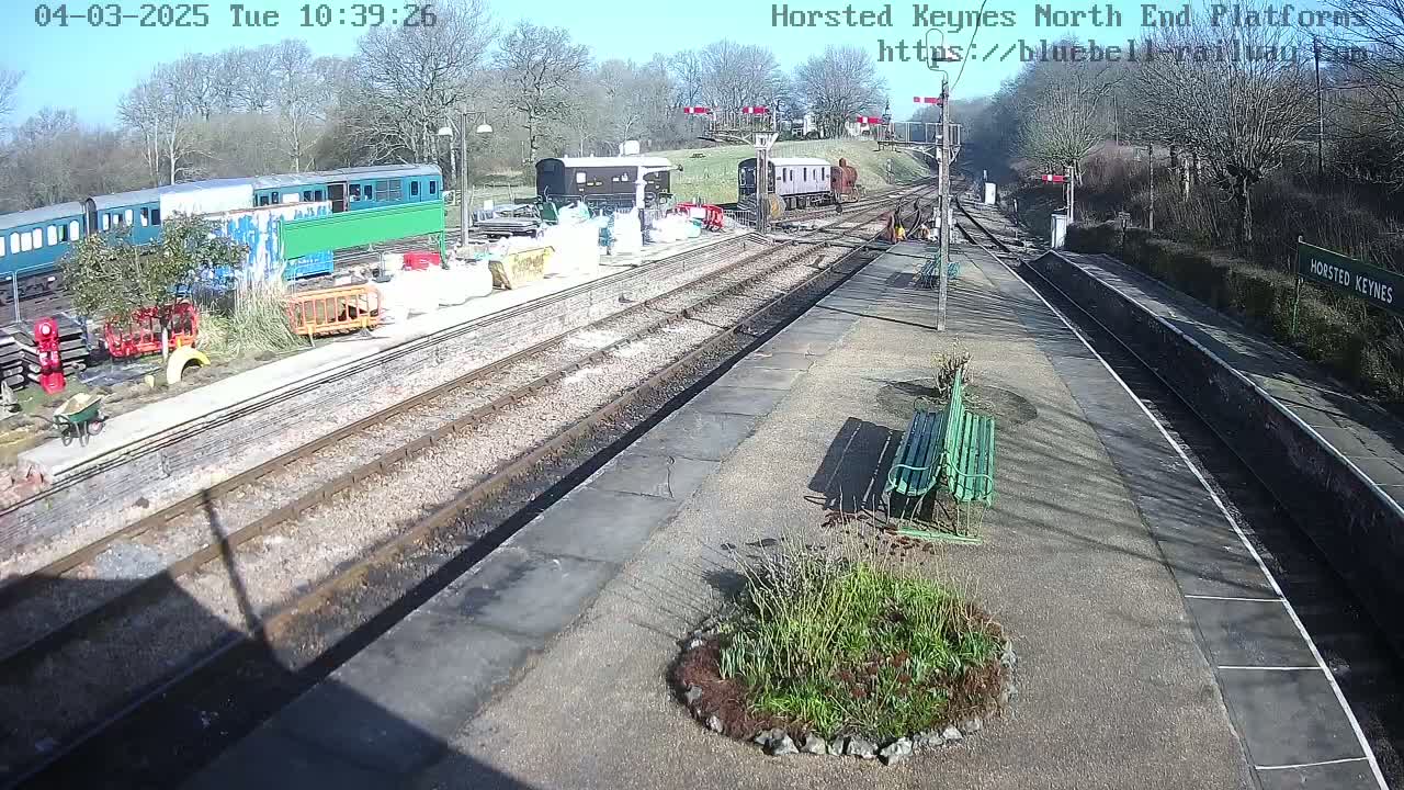 A sunny day at a train station with several railway carriages, construction materials, and a small garden visible.