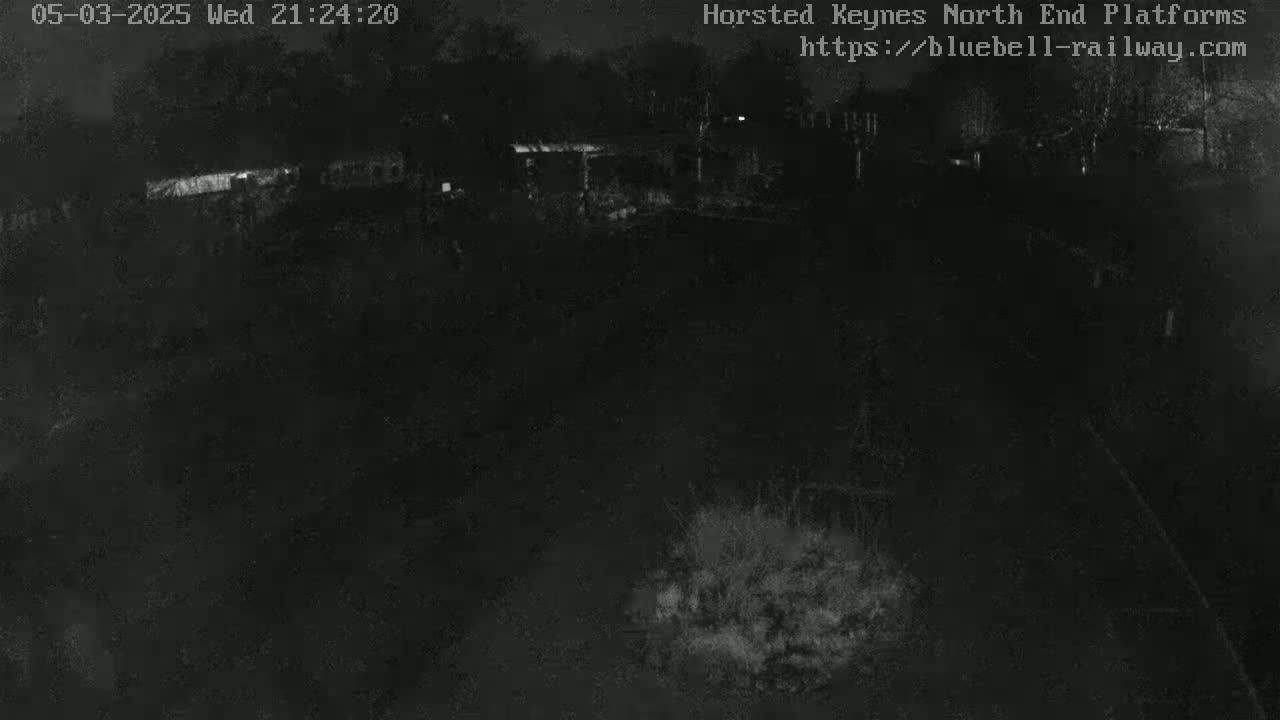 A dark, nighttime view of an empty area with some indistinct structures in the distance.
