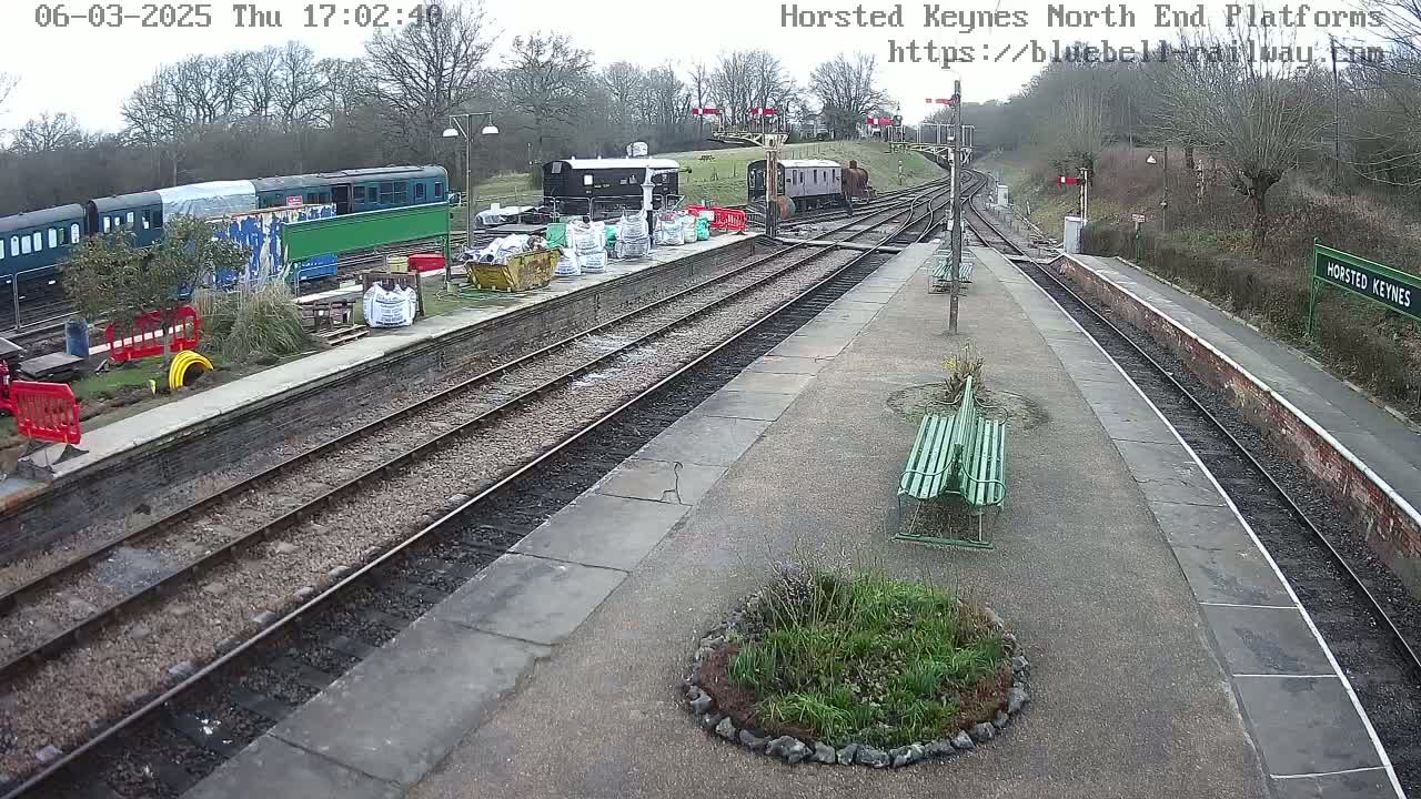 A train station with multiple train cars and railway tracks, under an overcast sky.