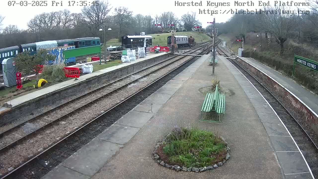 A train station platform with several train cars and construction materials visible under an overcast sky.