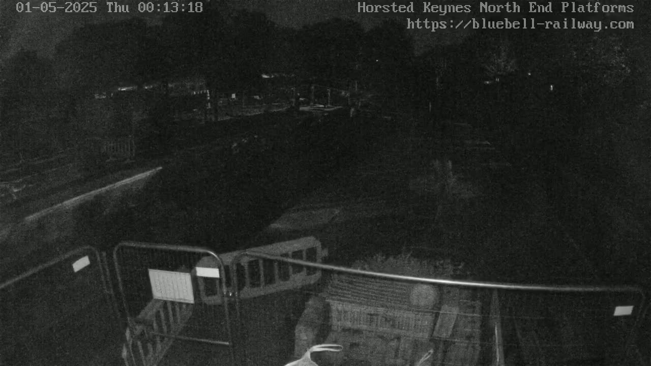 A nighttime low-light image shows a dark, empty area with metal barriers and what appears to be construction or maintenance equipment.