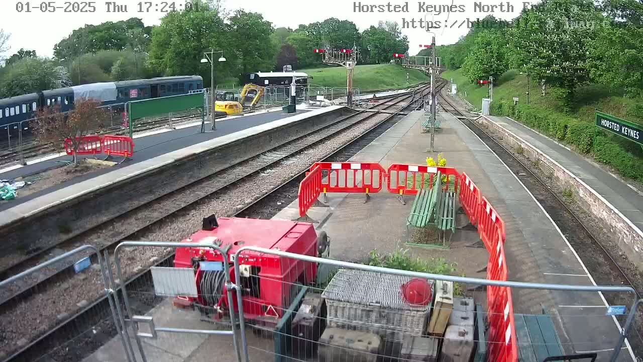 A train sits in a station undergoing railway construction, under a partly sunny sky.