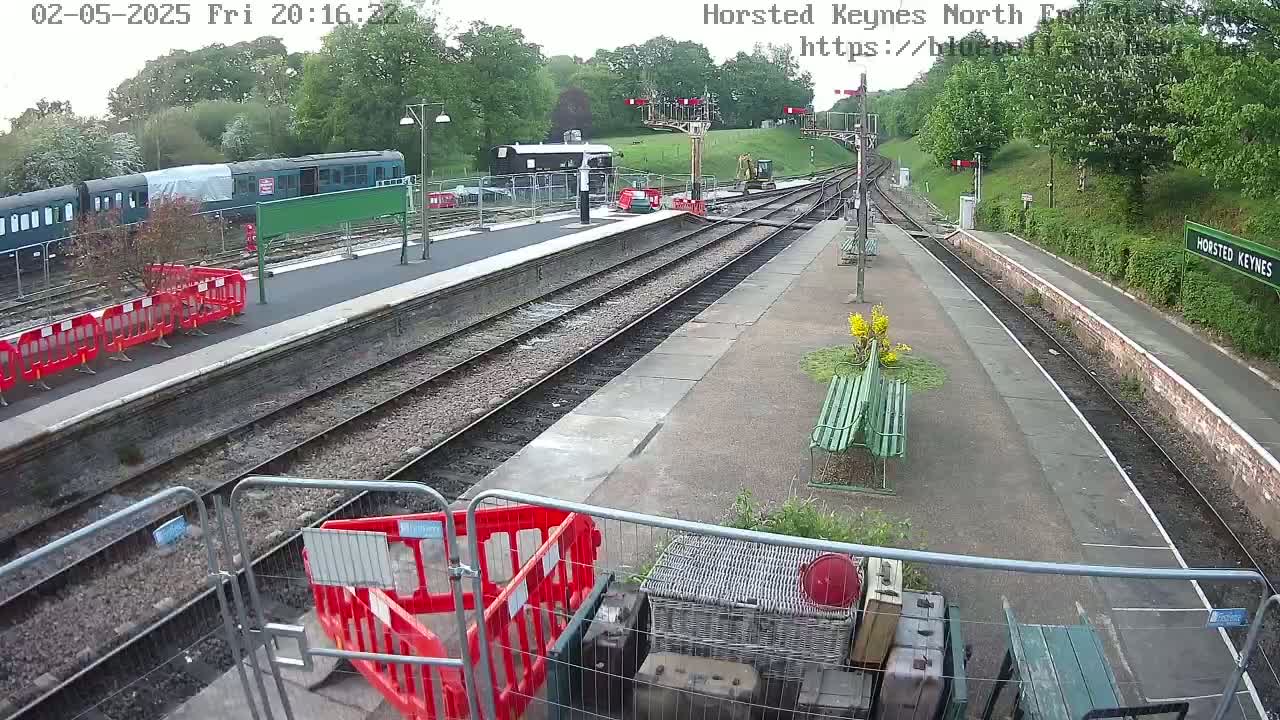 A train station platform with railway tracks, partially covered by construction fencing and barriers, under daytime conditions.