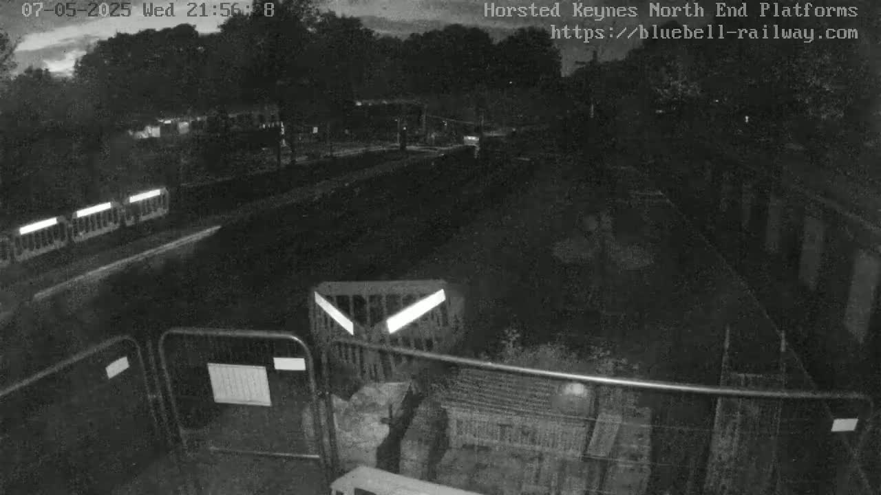 A nighttime, low-light view of a mostly empty, fenced-off area with some barriers and what appears to be construction materials.