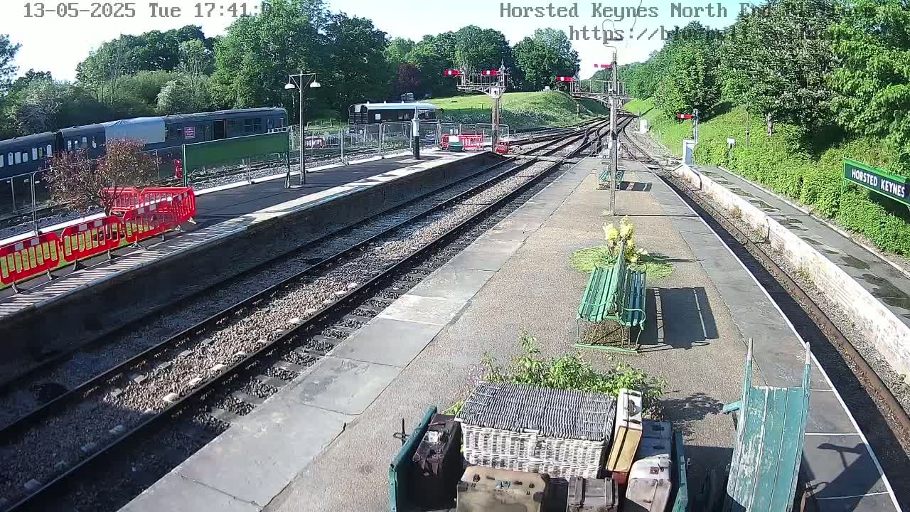 A train sits at a station platform on a sunny day, with railway tracks extending into the distance.