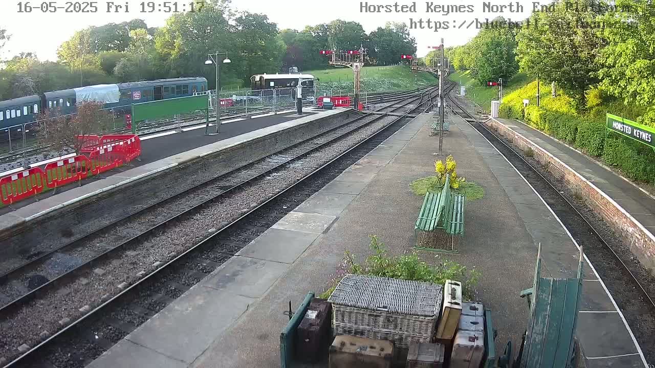 A train sits at a railway station platform under a clear evening sky, with several parallel train tracks extending into the distance.