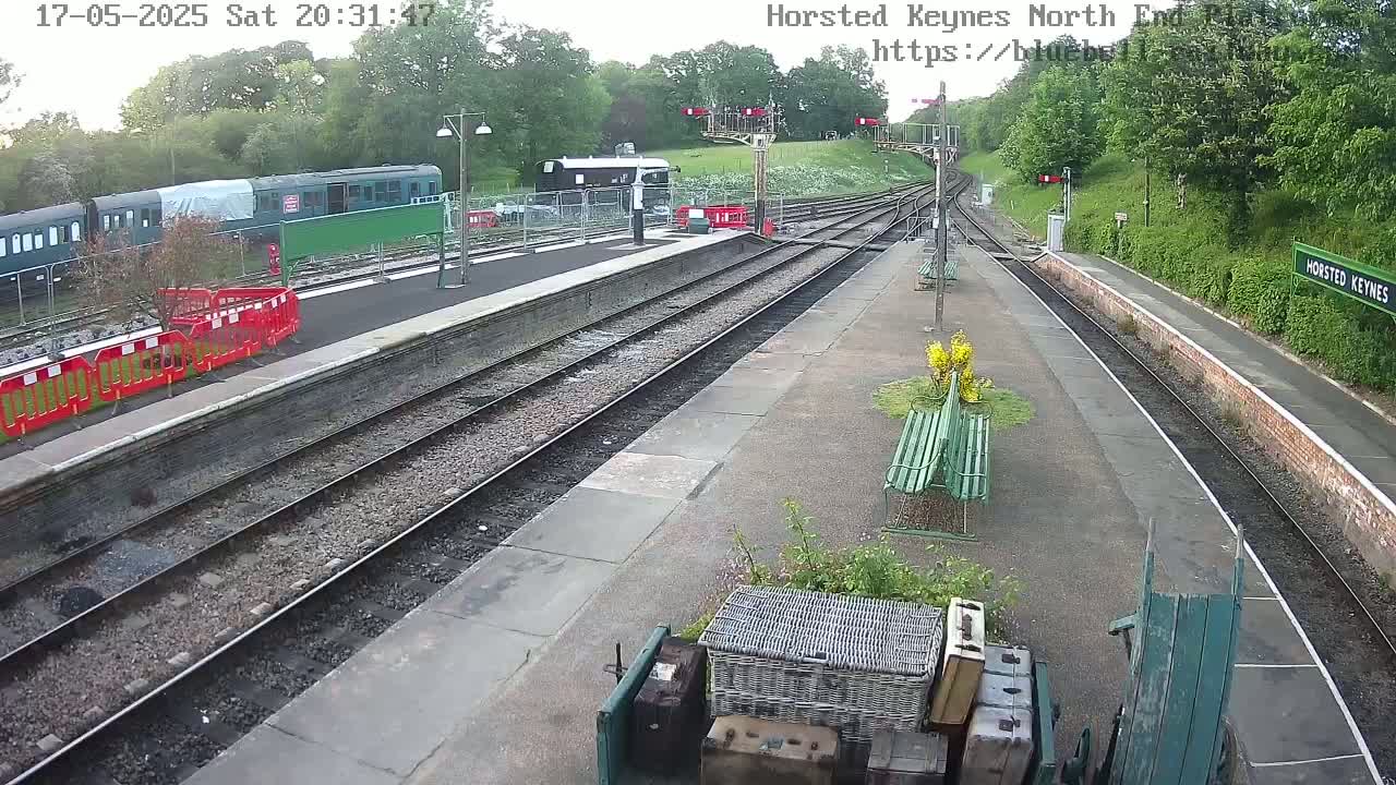 A mostly empty train station platform with several train cars visible in the distance, under an overcast sky.
