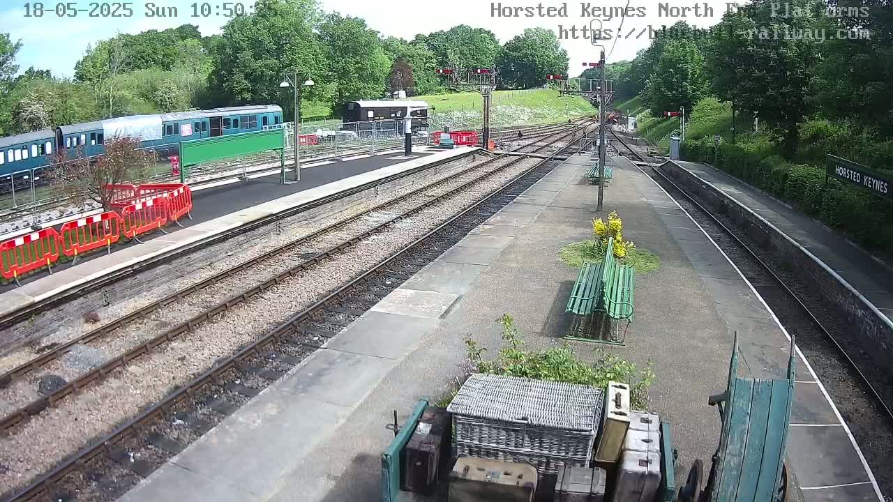 A sunny day at a train station with multiple train cars parked on the tracks and several benches on the platform.