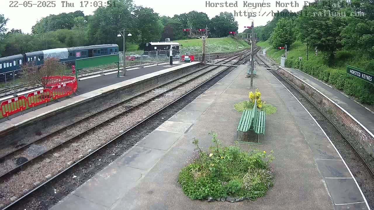 A train station platform with multiple train cars visible, under a partly cloudy sky.
