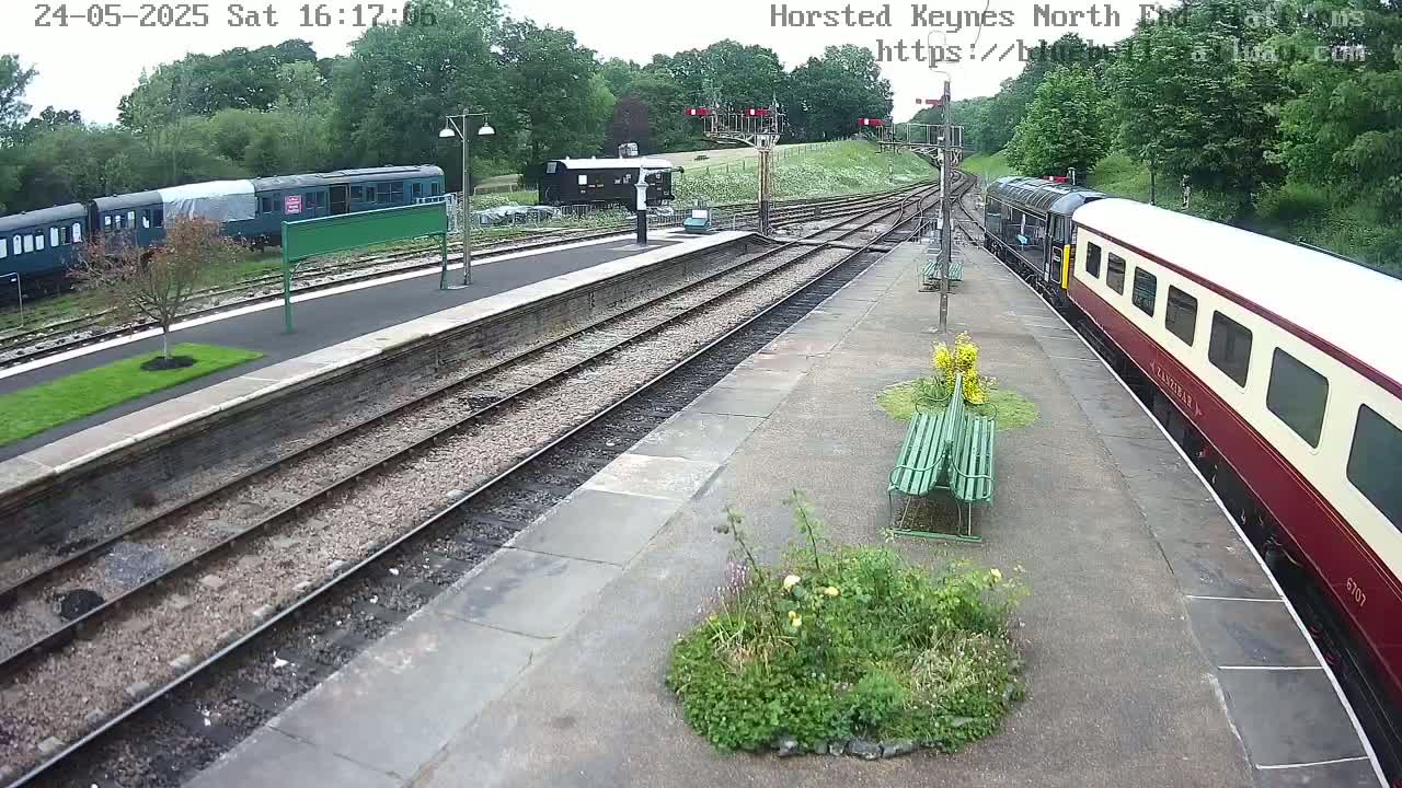 A train station on an overcast day with multiple train cars on the tracks, including a maroon and cream passenger car.