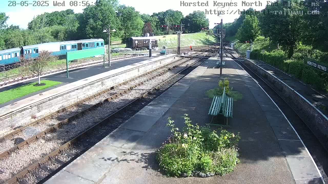 A sunny day at a train station with several train cars parked on the tracks, and a few people visible in the distance.