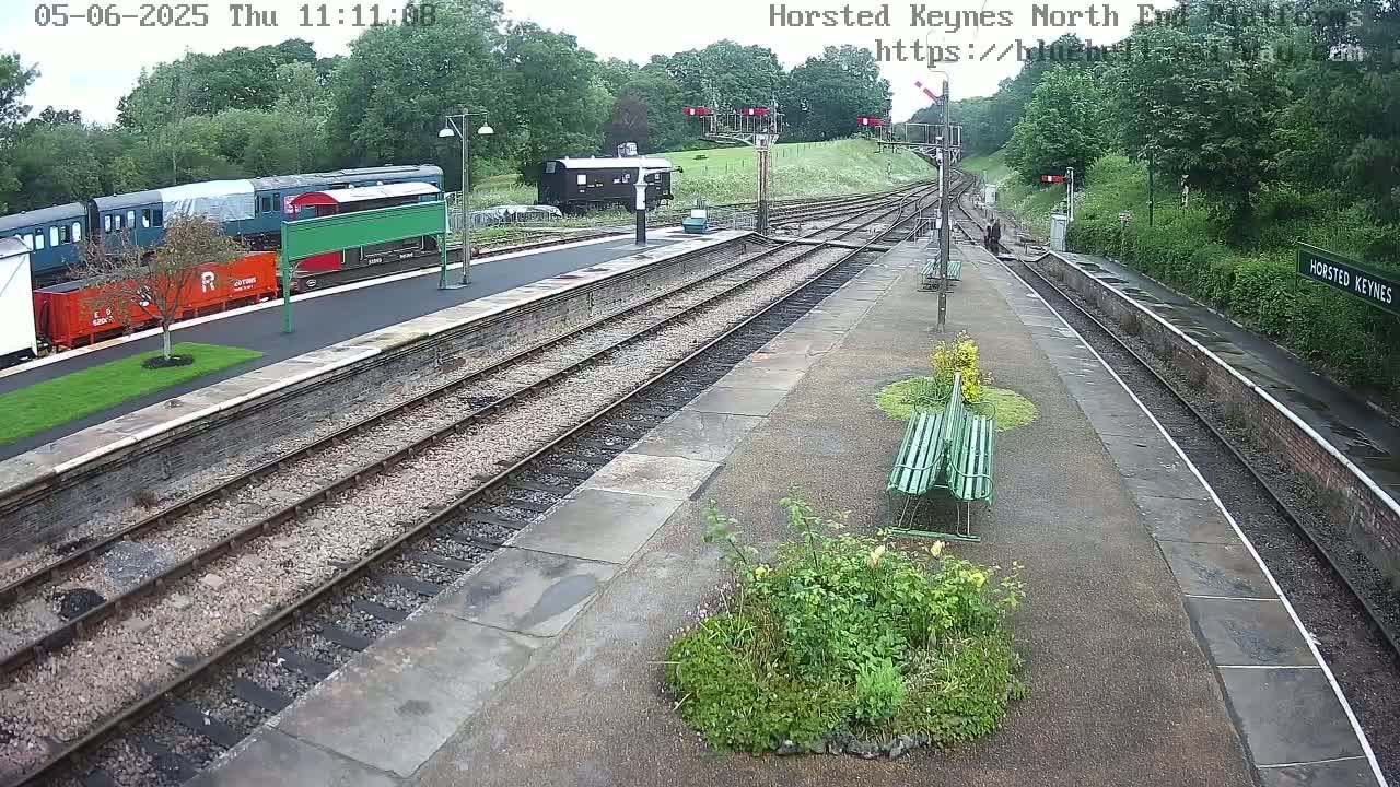 A railway station platform with several train cars parked on the tracks, under an overcast sky.