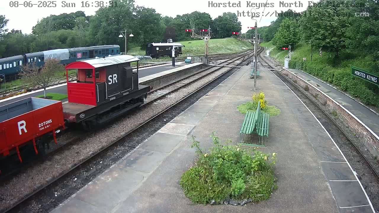 A railway station platform with several train cars, including a red and black one, under an overcast sky.