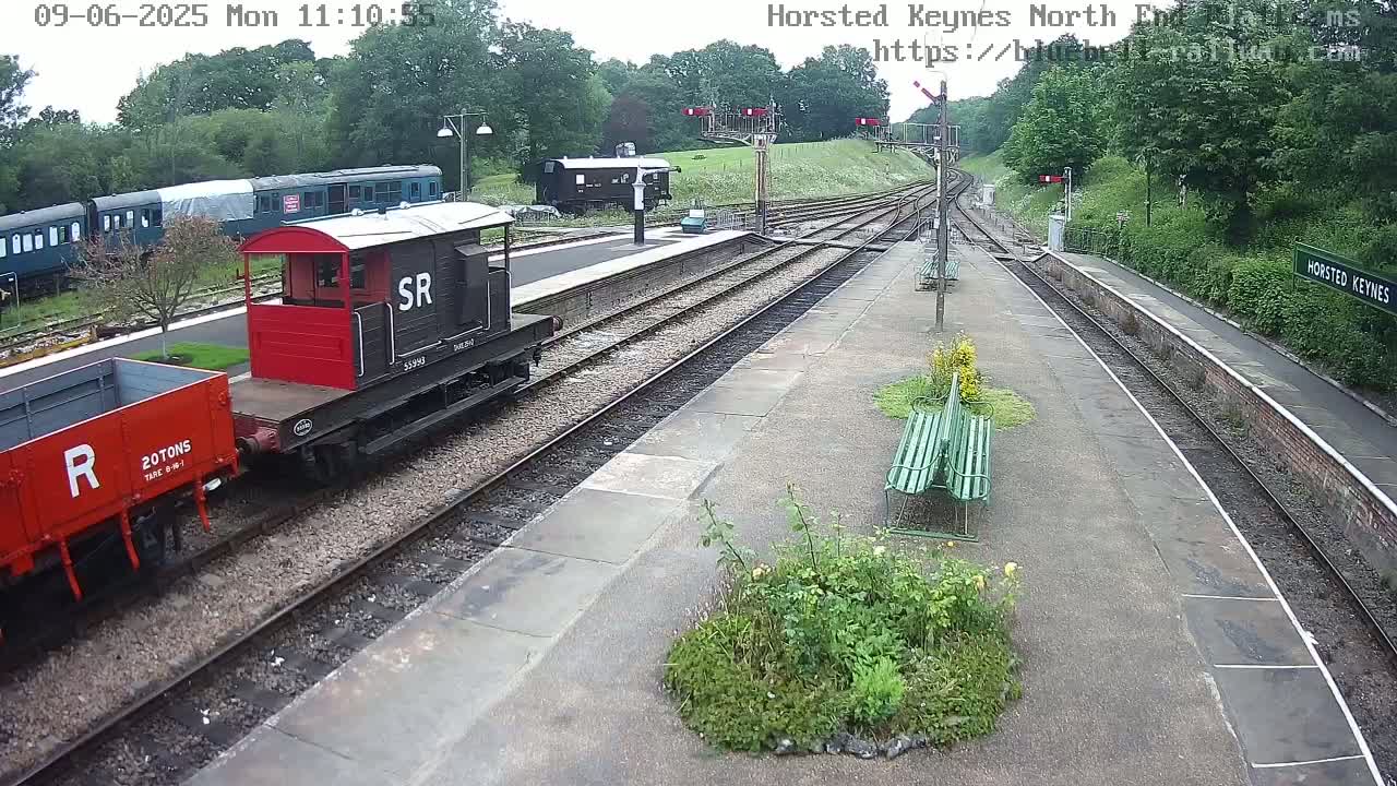 A railway station platform with several train cars and a small diesel locomotive parked on the tracks on an overcast day.