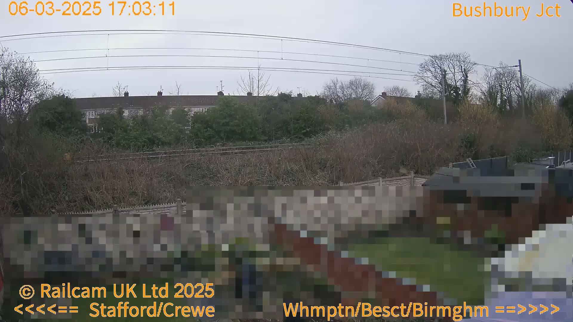 A view of a residential area and railway tracks on an overcast day, seen from a backyard perspective.
