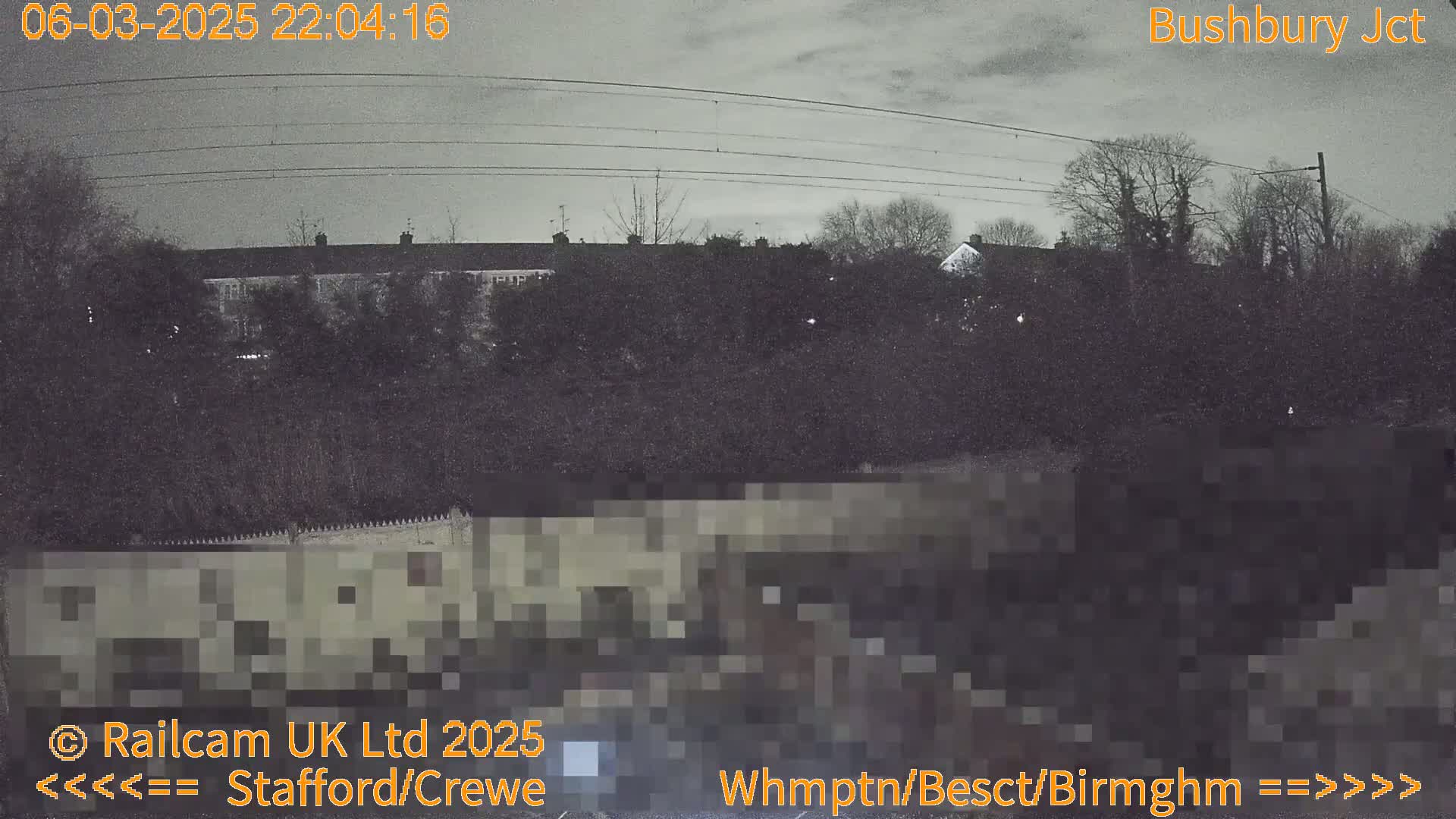 A nighttime view of a row of houses behind a wall and some trees under a cloudy sky.