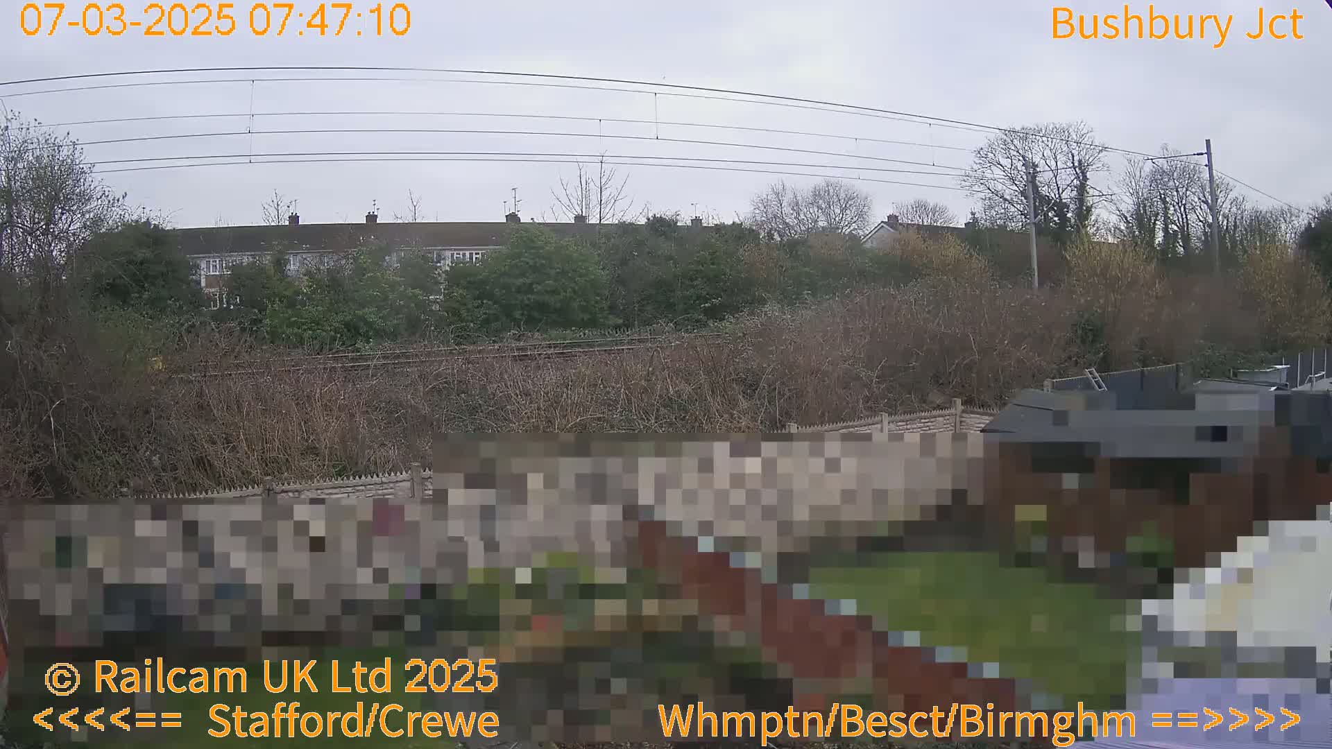 A view of a residential area with train tracks and overhead power lines under an overcast sky.