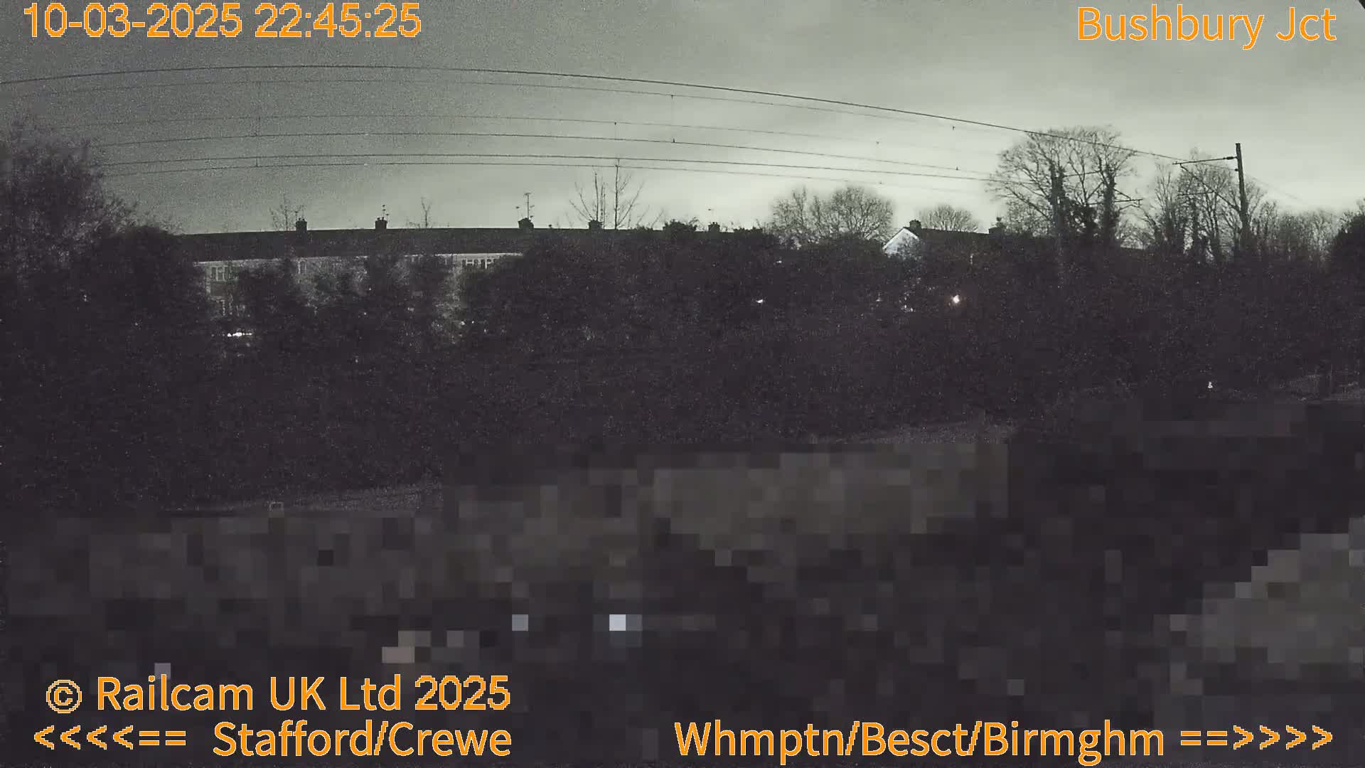 A nighttime, overcast view of residential buildings and trees, seen from across a road or railway line.