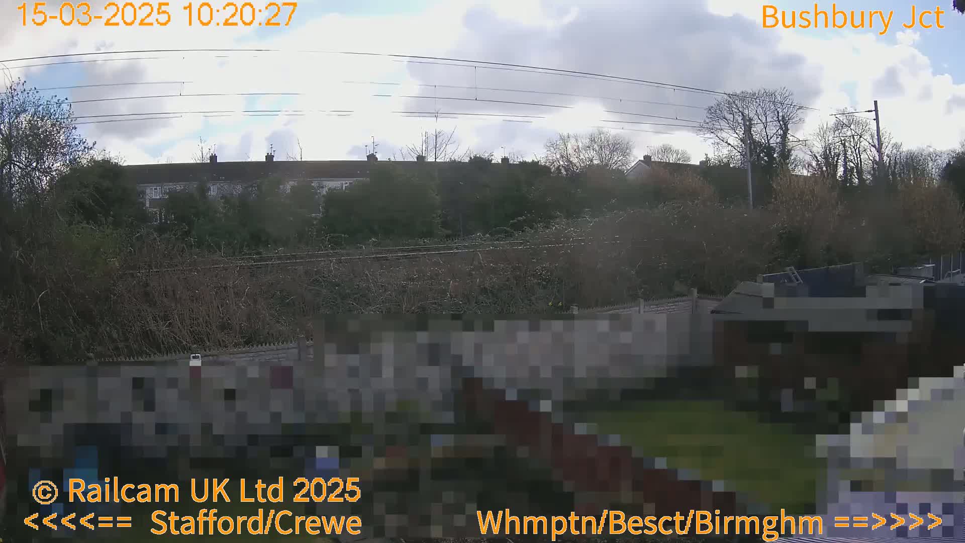 A partly cloudy sky over a residential area with trees and a fence, viewed from a backyard.