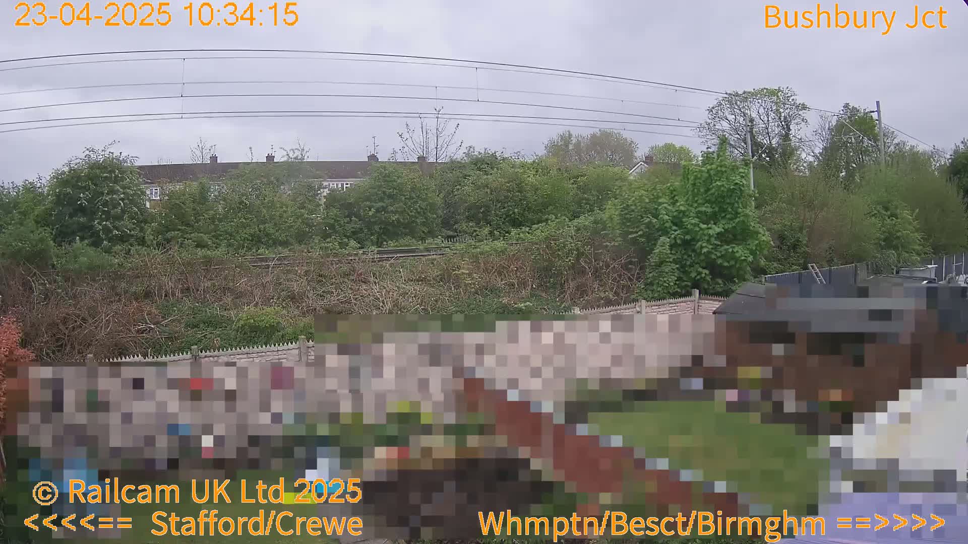 A view of a backyard with a fence and shed, overlooking a railway line and houses under an overcast sky.