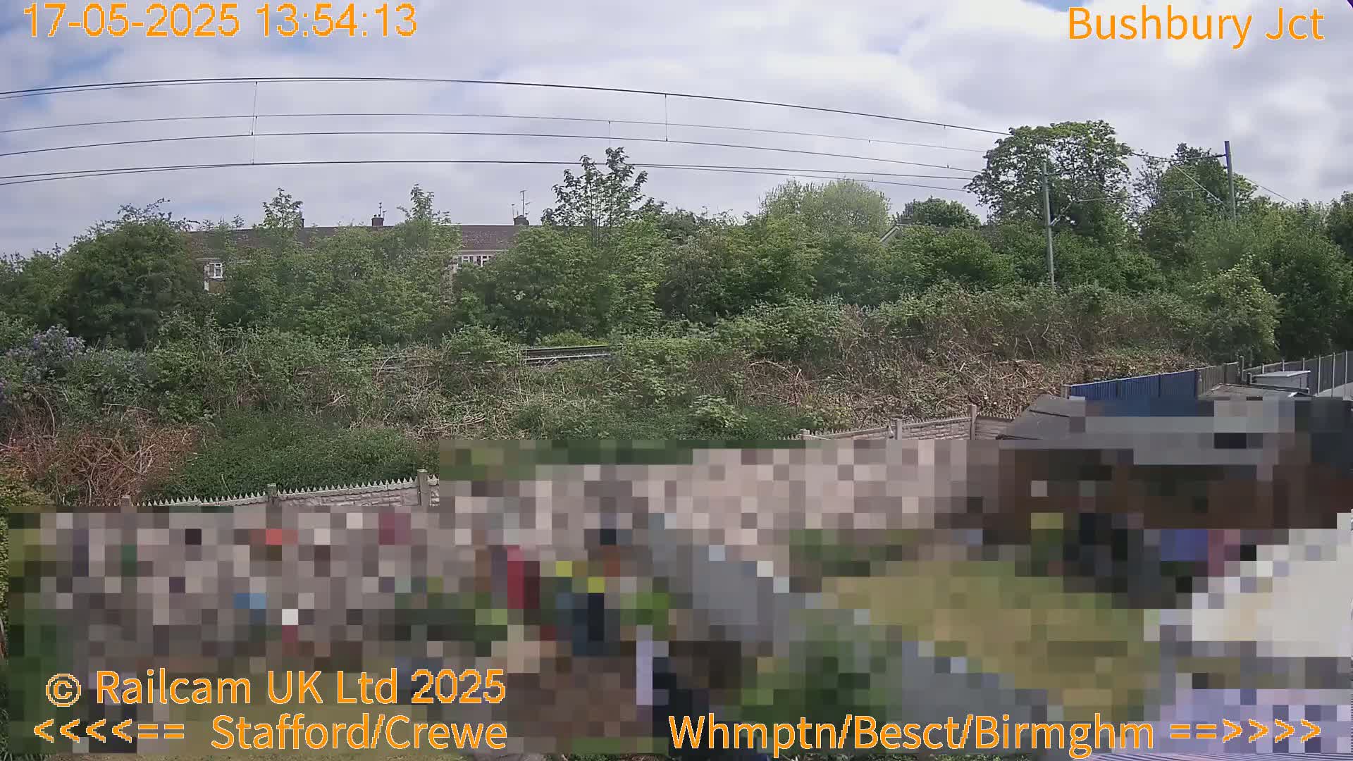 A view of a backyard garden next to a railway line under a partly cloudy sky.