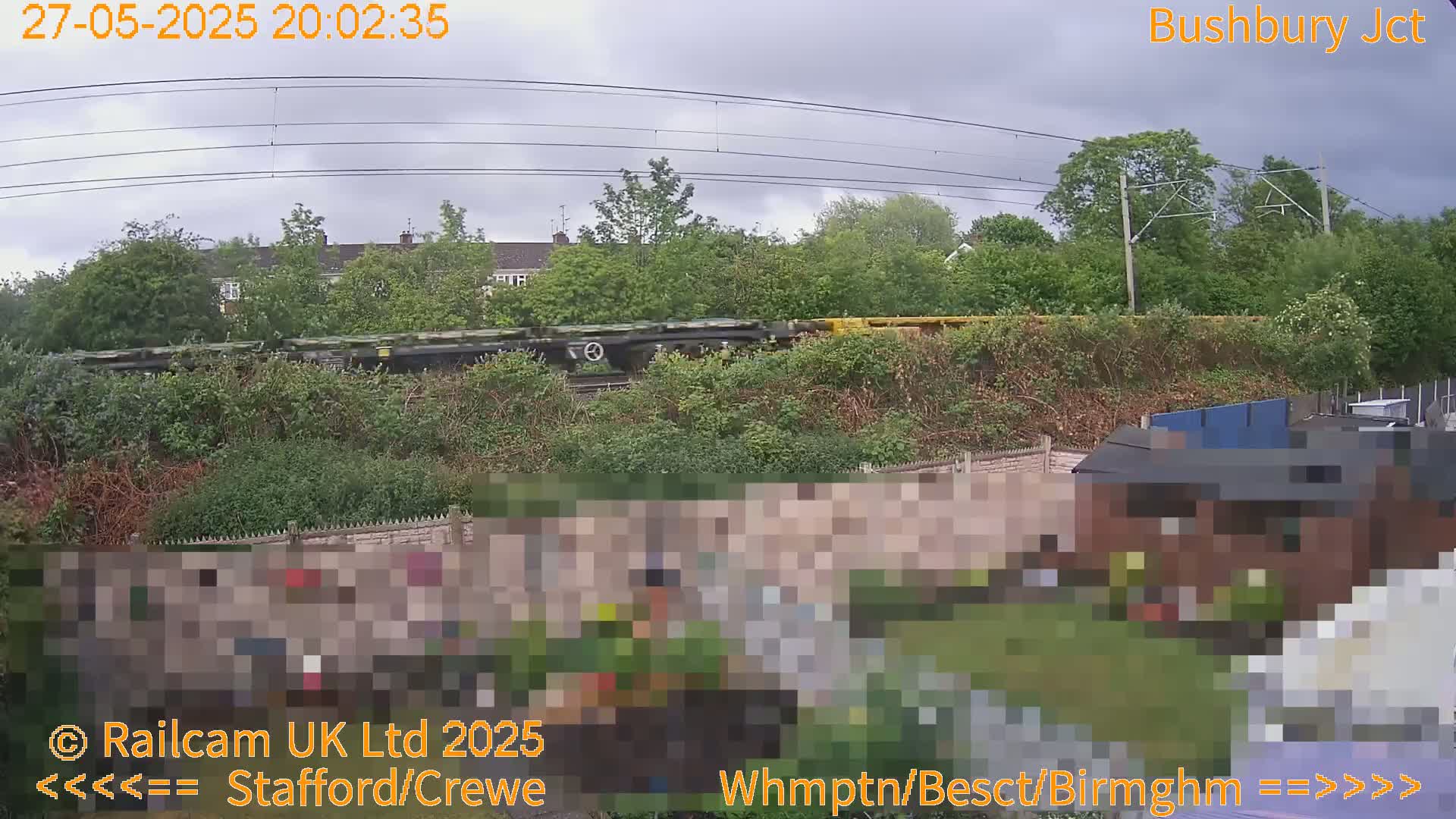 A freight train passes behind a garden wall on an overcast day.
