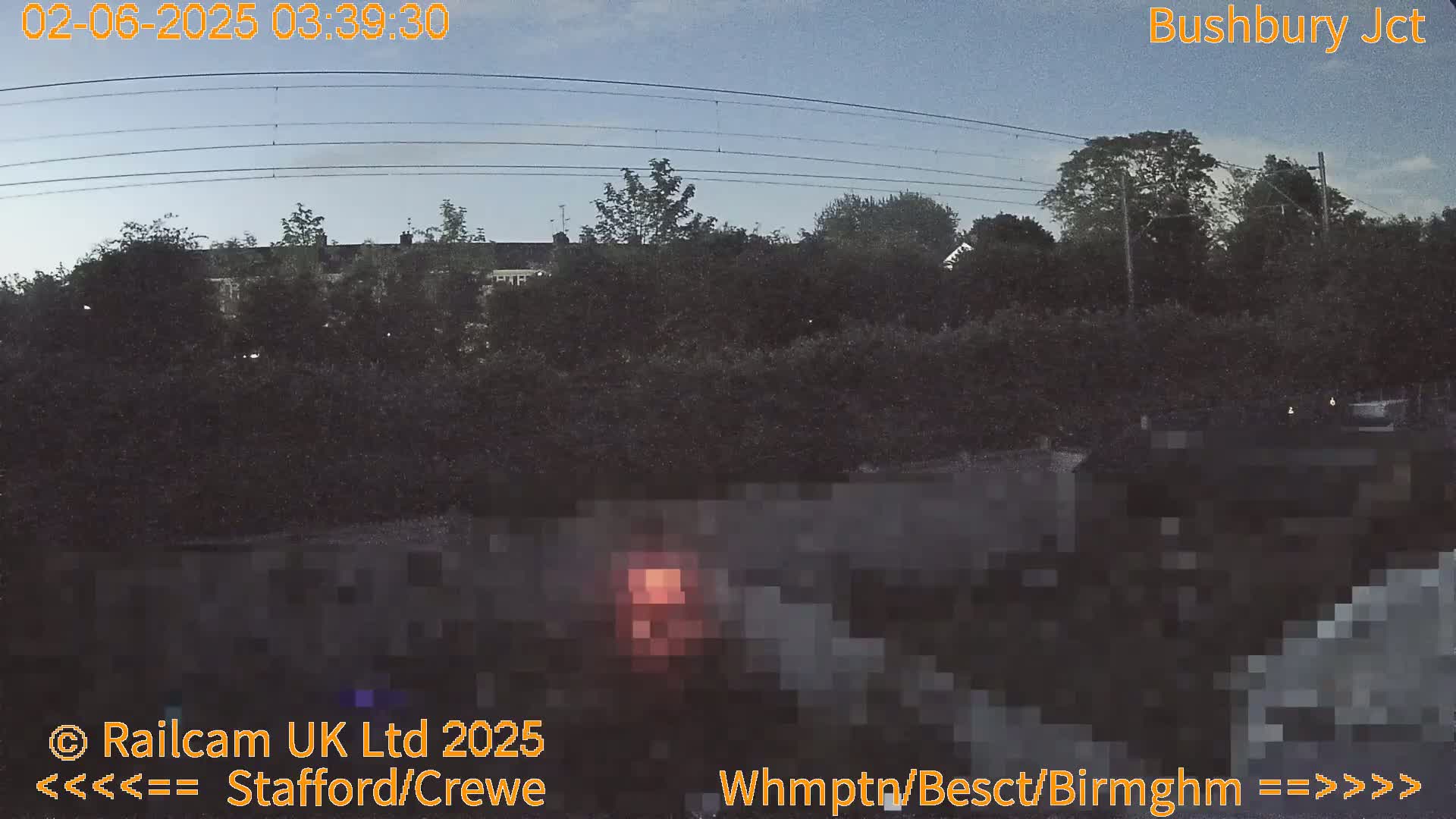 A low-light, nighttime view of trees and houses near a railway line under a mostly clear sky.