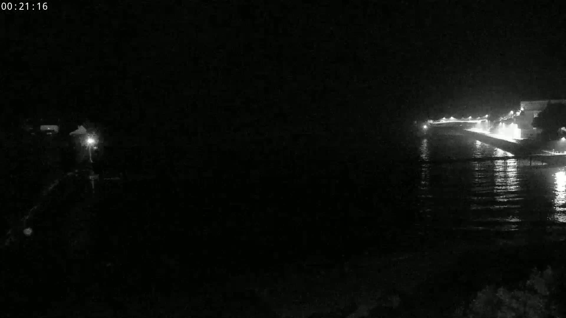 A nighttime, low-light view shows a dark body of water reflecting lights from a distant shoreline.