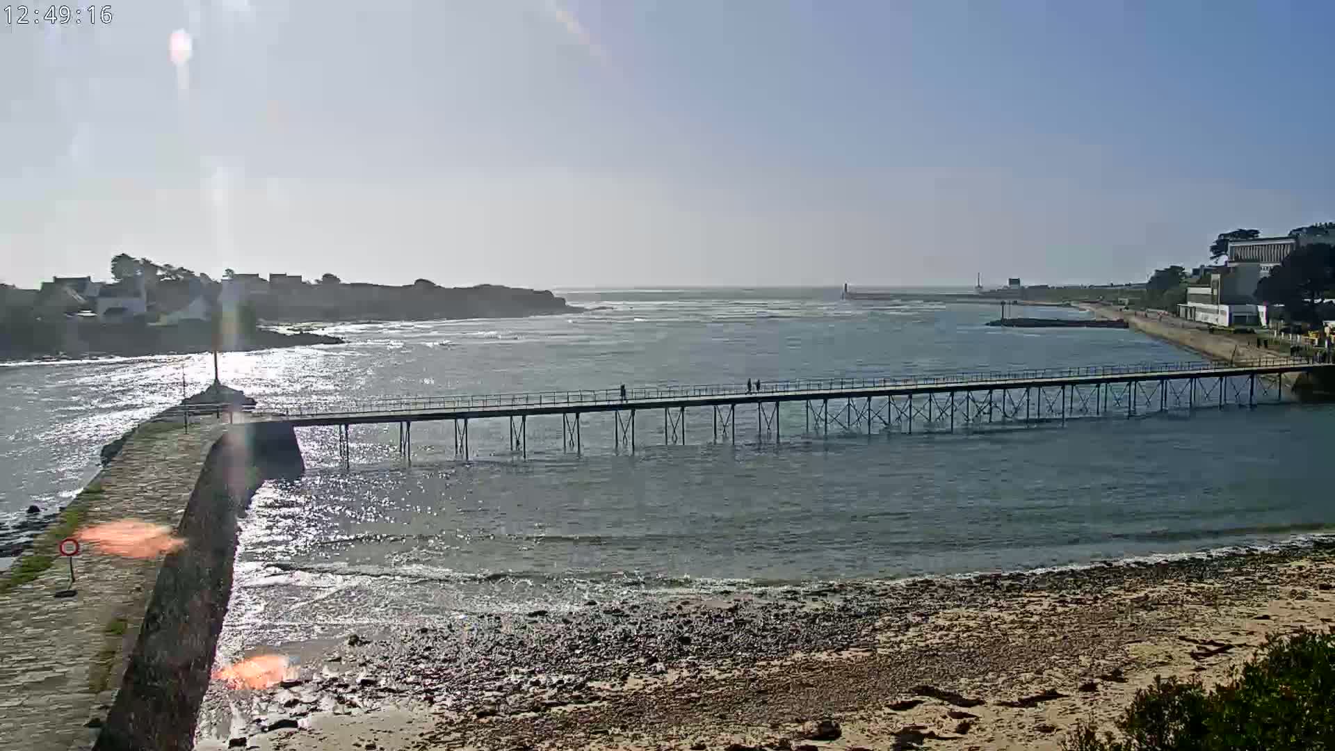 A long pier stretches across calm water toward a distant shoreline under a bright, sunny sky.