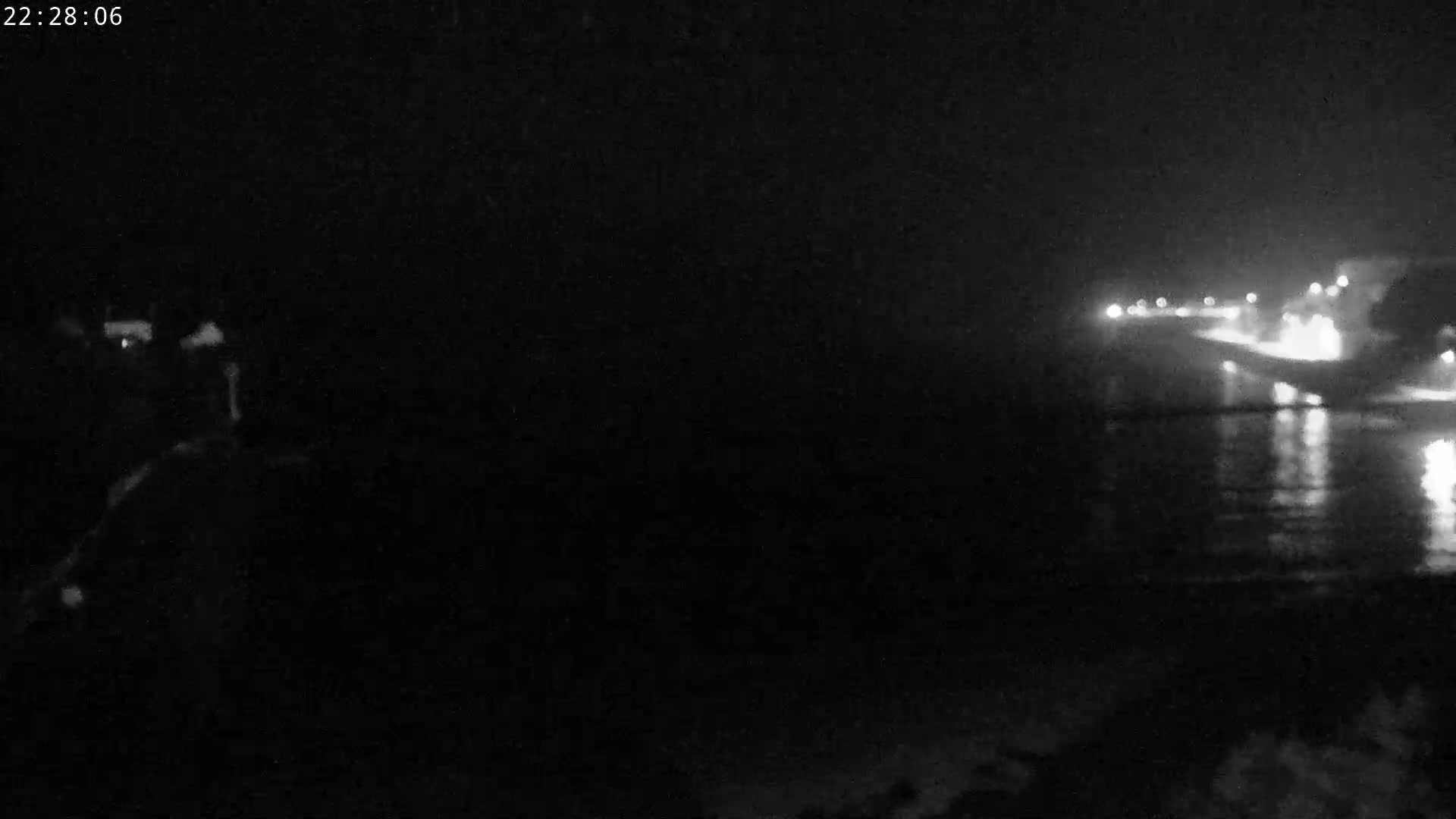 A nighttime, low-light view of a dark shoreline with a body of water reflecting distant lights.