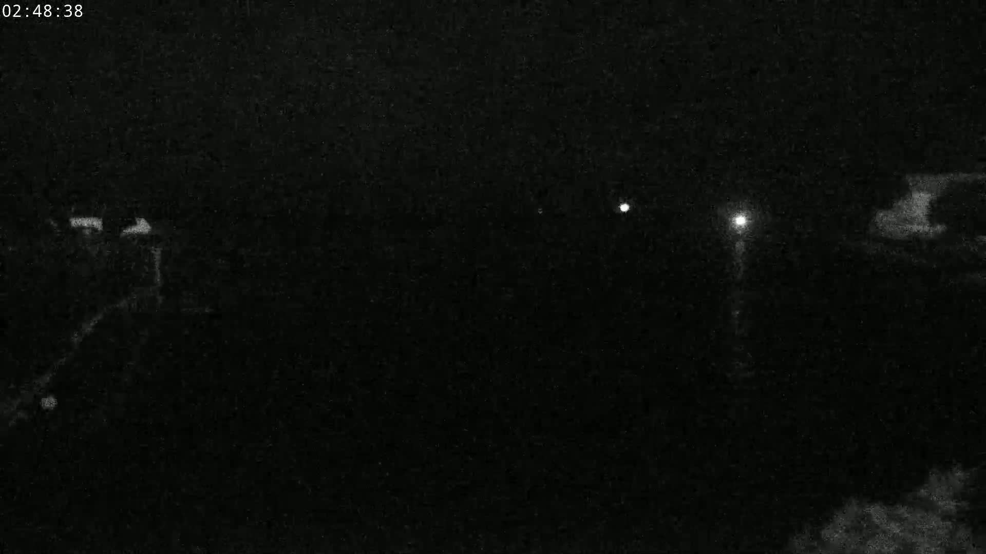A nighttime, low-light image shows indistinct shapes and a few faint lights in the distance.