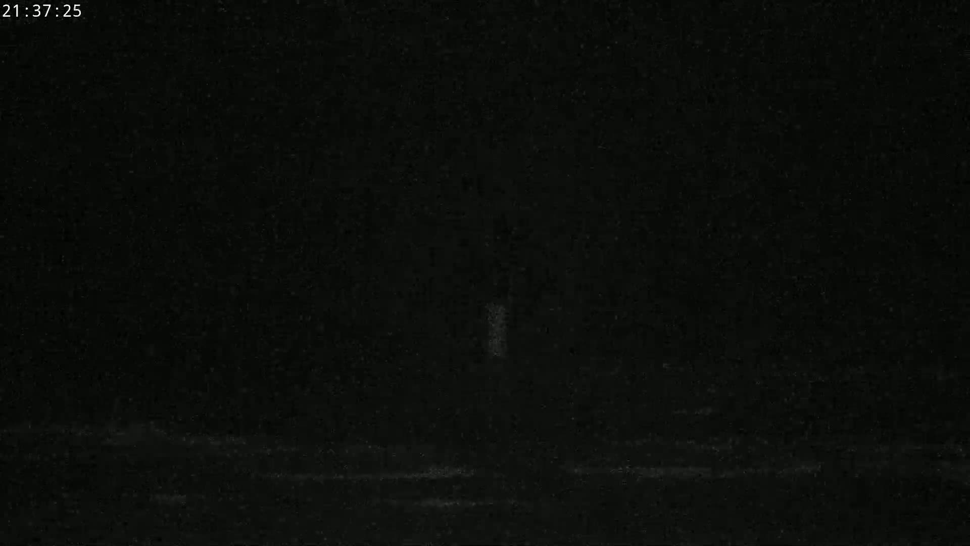 A nighttime, dark image shows a faintly lit, vertical structure in the center, with a dark, possibly snowy or dusty ground below.