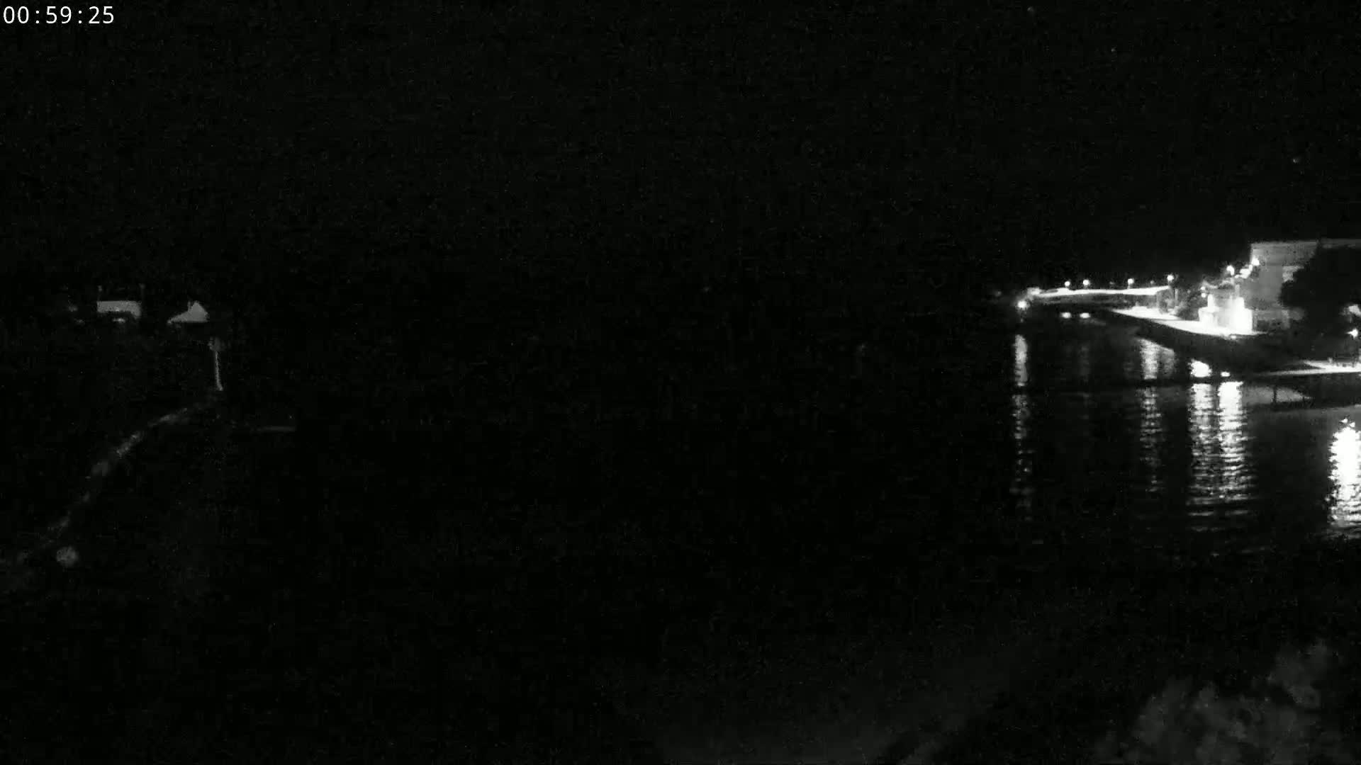 A nighttime, low-light view shows a dark body of water reflecting lights from a distant shoreline.
