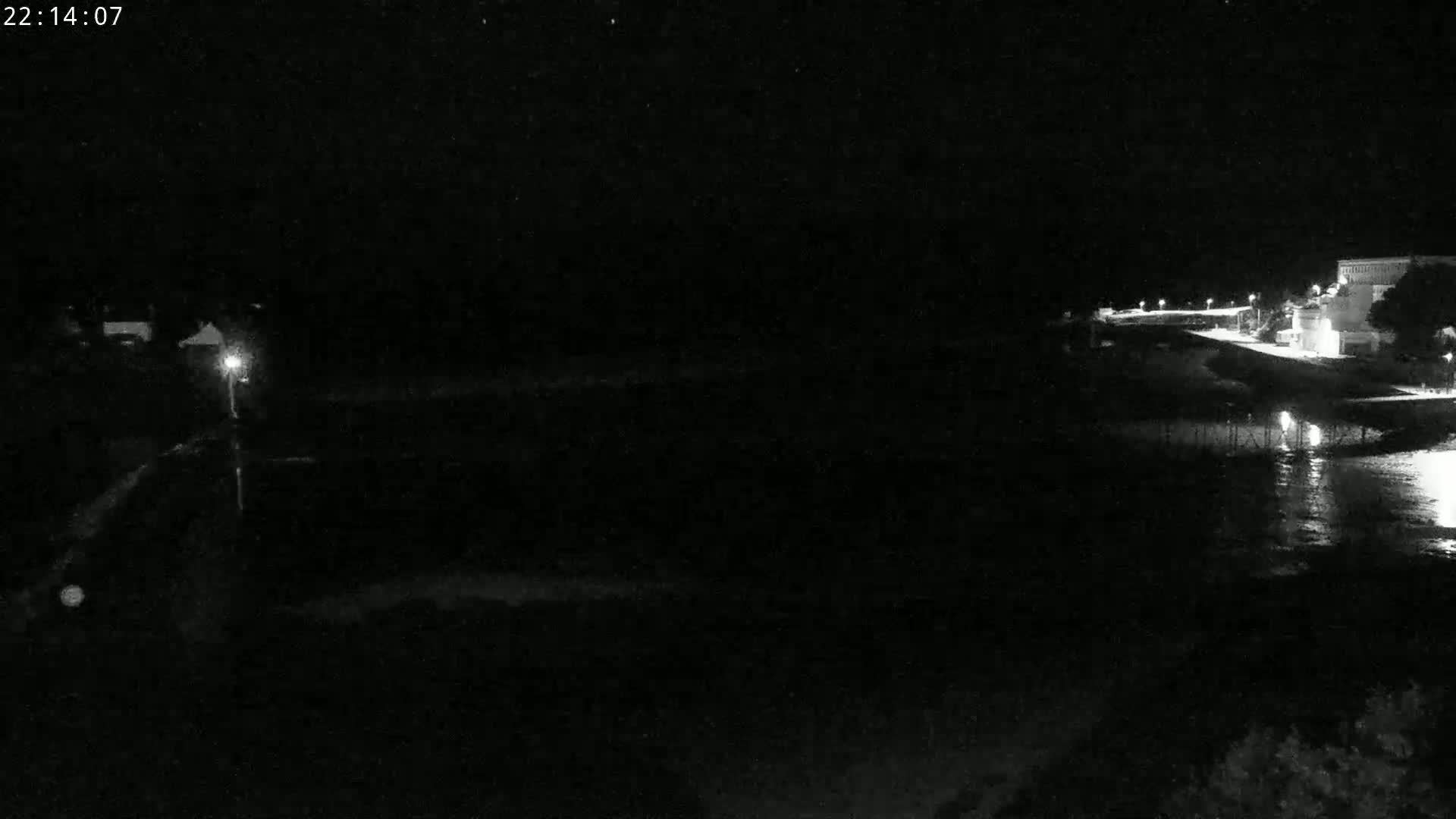 A nighttime, low-light view shows a dark body of water reflecting lights from a nearby building and shoreline.