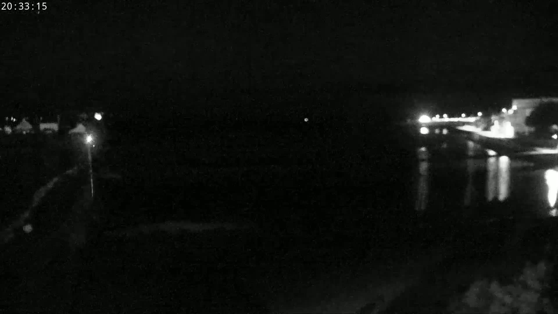 A nighttime, low-light image shows a dark body of water reflecting lights from a distant shoreline.