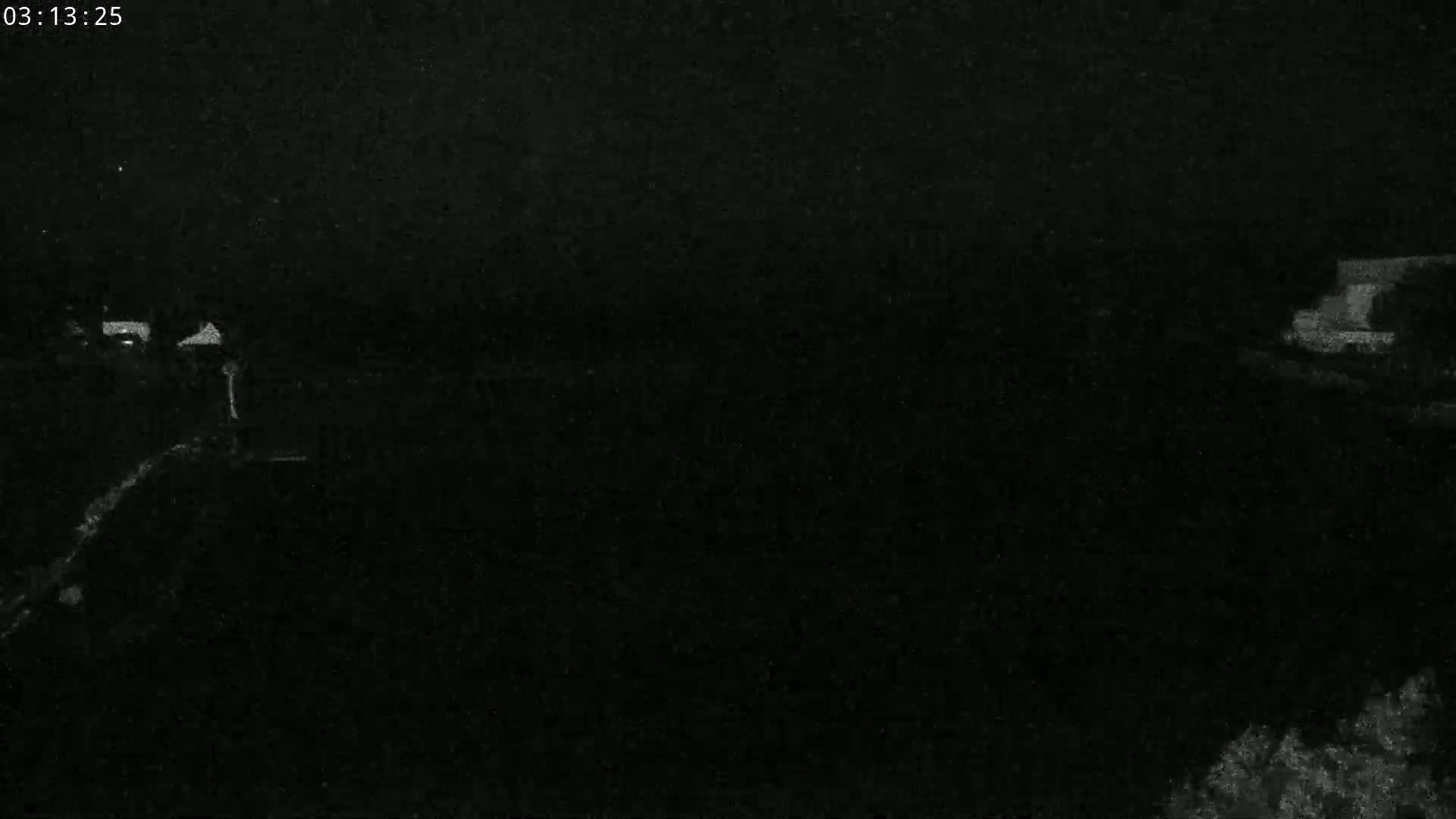 A low-light, nighttime image shows a dark, possibly rural landscape with indistinct structures in the distance.