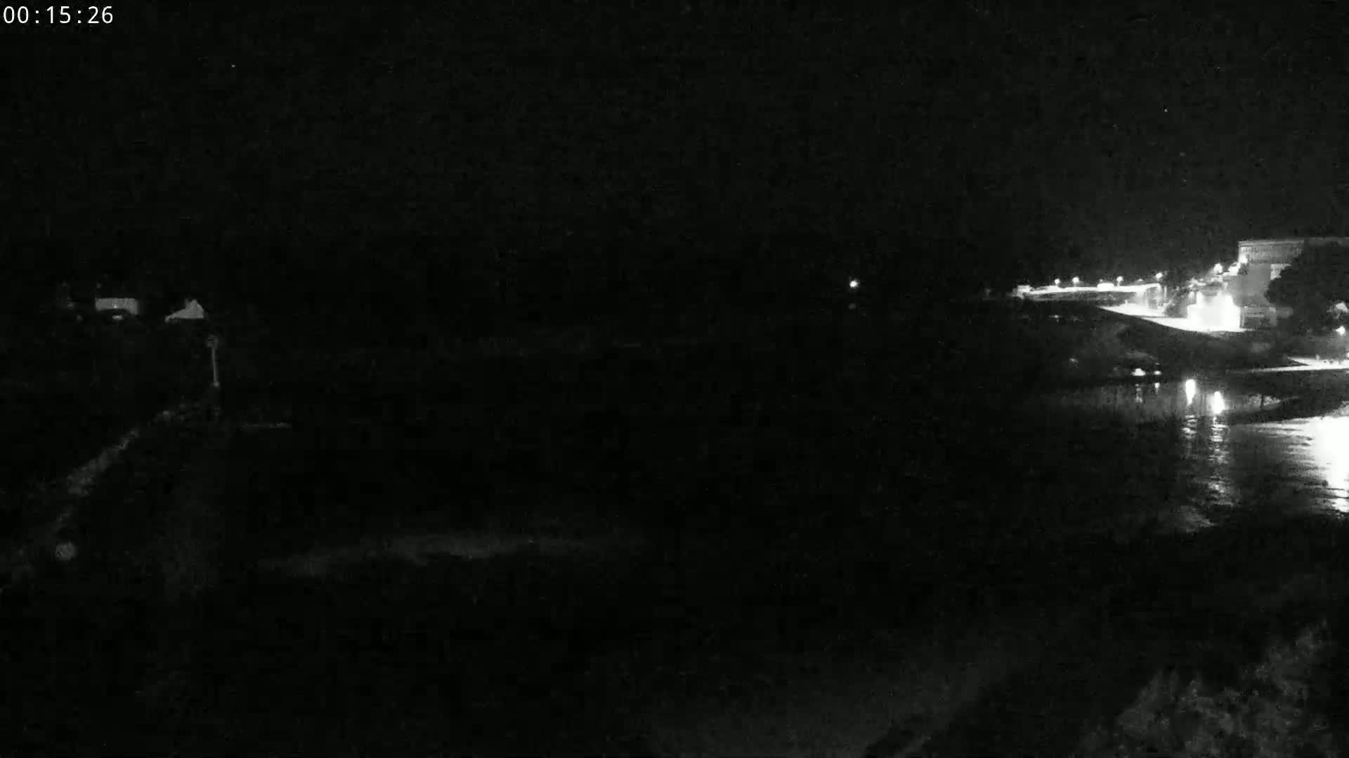 A nighttime, low-light view of a dark body of water next to a dimly lit shoreline with buildings.