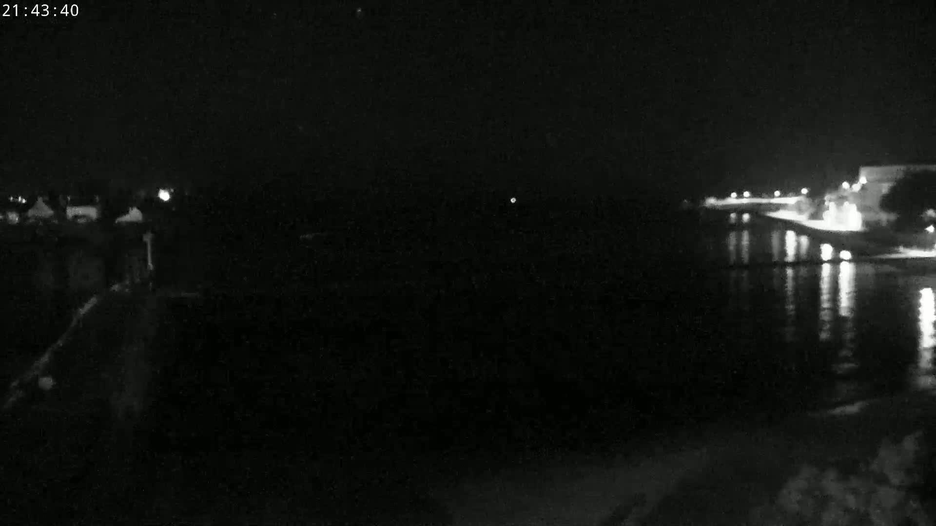 A nighttime view of a dark body of water reflecting lights from a distant shoreline.
