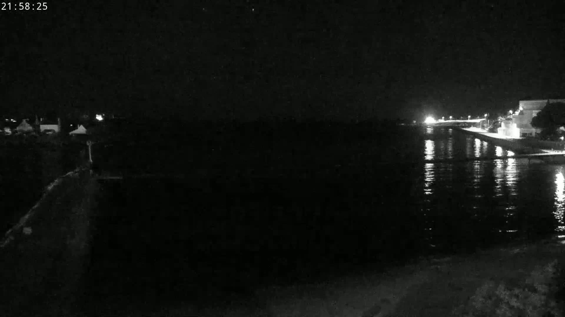 A nighttime, low-light view of a calm body of water reflecting lights from a shoreline with buildings.