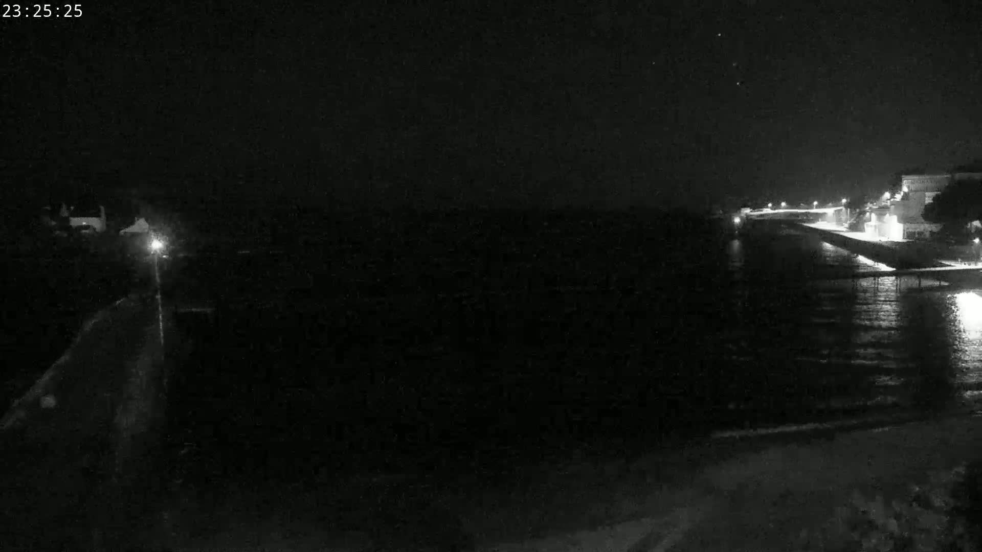 A nighttime view of a dark body of water with a dimly lit pier and shoreline in the background.