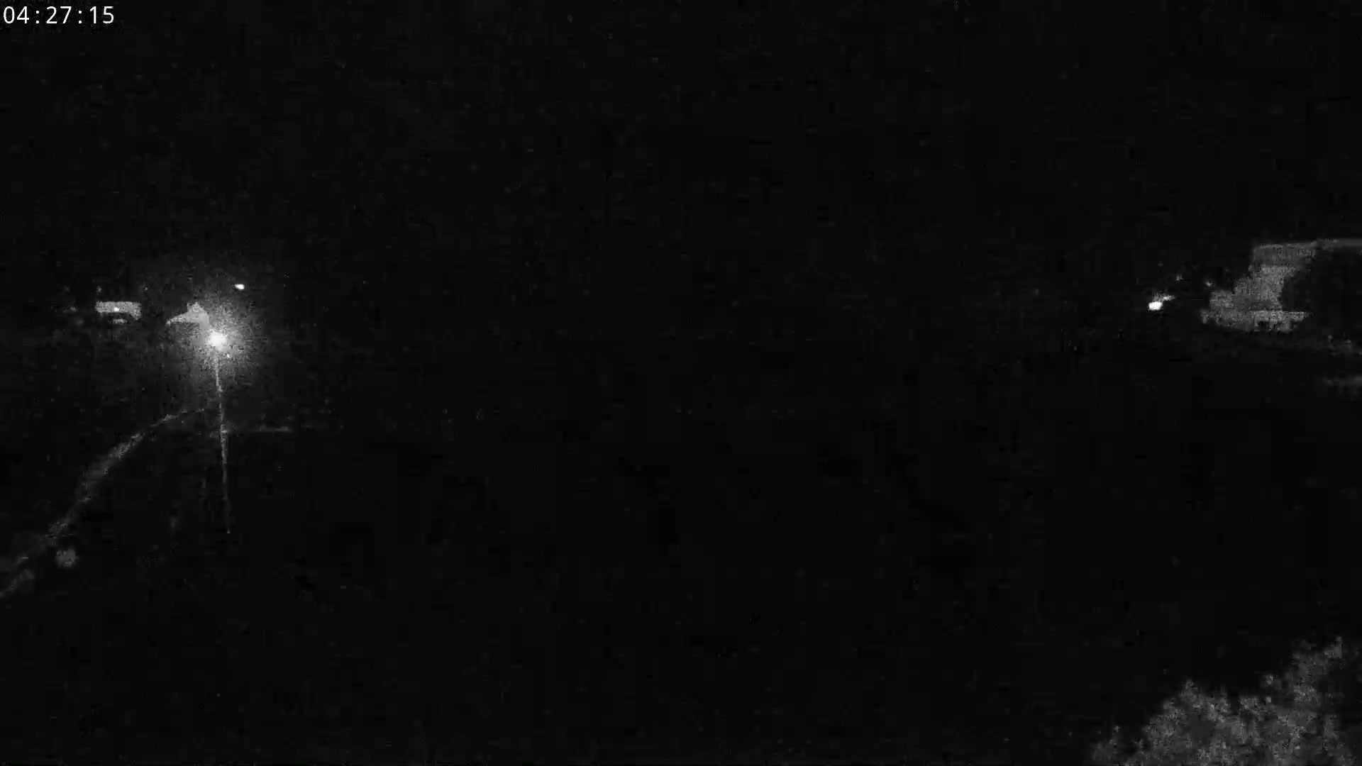 A nighttime, low-light image shows a dark road with faint lights visible in the distance.