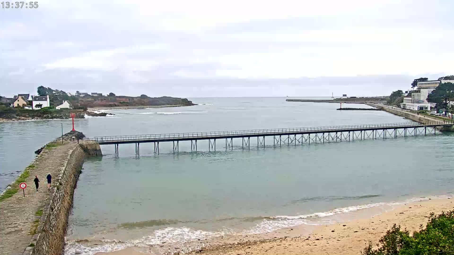 A long pier stretches across calm, light-green water toward a small town under an overcast sky.
